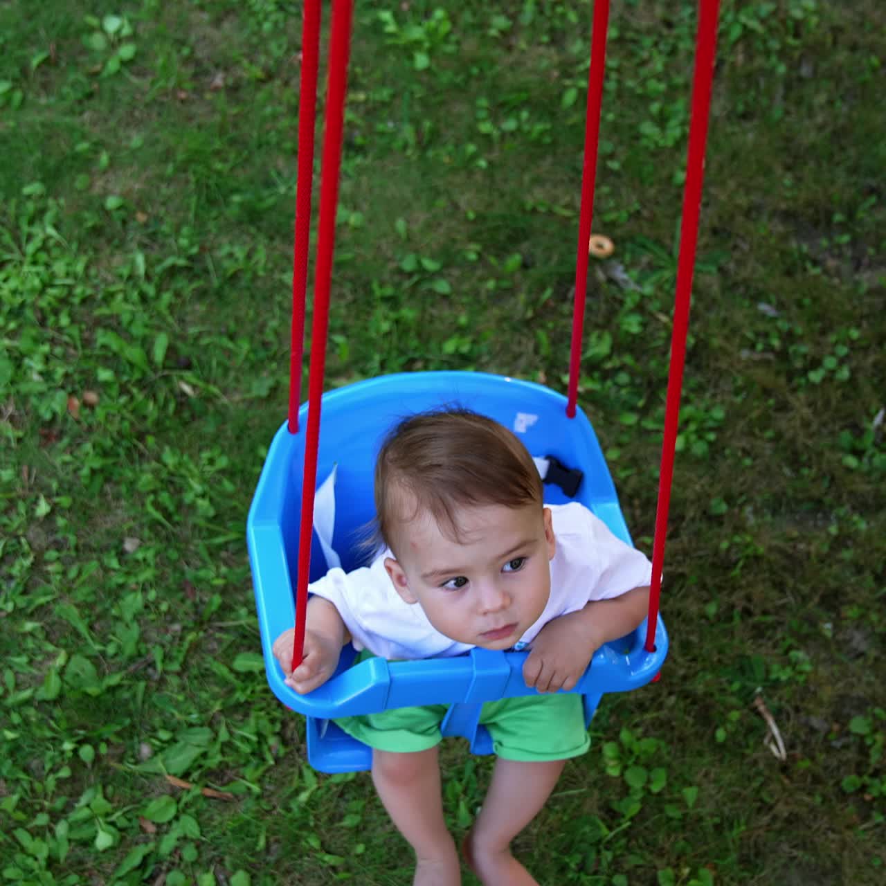 Thoughtful little baby sitting in a blue swing and swaying. Summer in the village concept. View from above