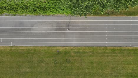 Top-down-aerial-view-of-person-skateboarding-through-frame-along-a-grey-running-track