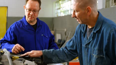 Mechanic-examining-a-car-while-his-colleague-using-laptop-4k