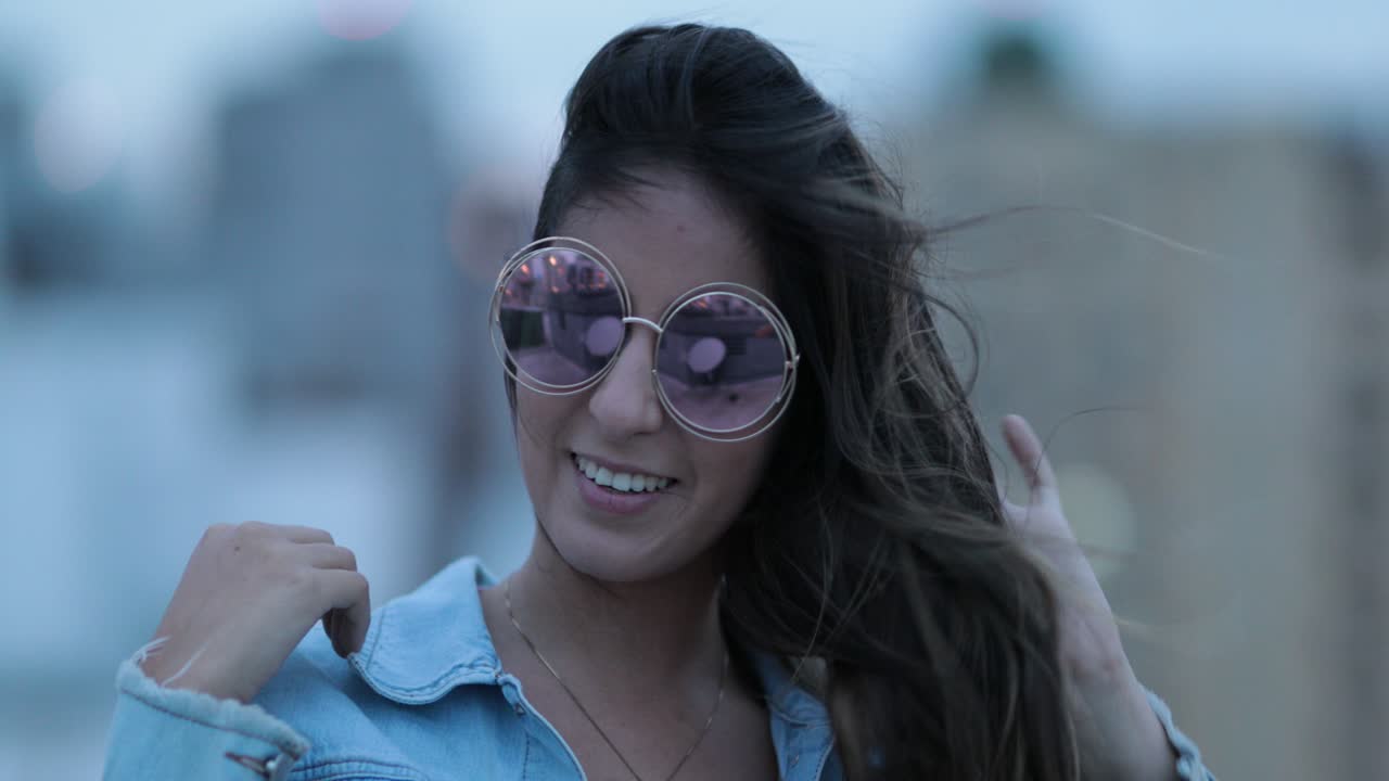 una mujer joven posando con grandes gafas de sol redondas y divertidas, el viento soplando el cabello