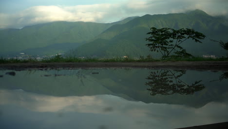 The-stunning-Lake-Kawaguchiko-in-Honshu,-Japan-showcases-lush-green-mountains-in-the-background,-reflecting-buildings-on-its-tranquil-waters,-epitomizing-the-serenity-of-the-lake