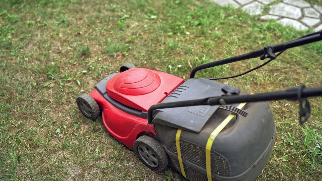 Red lawn mower in the garden. Boy is cutting grass by electrical mower machine outdoors.