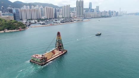 Tugboat-pulling-a-barge-loaded-with-fresh-excavated-Sand-along-Hong-Kong-coastline,-Aerial-view