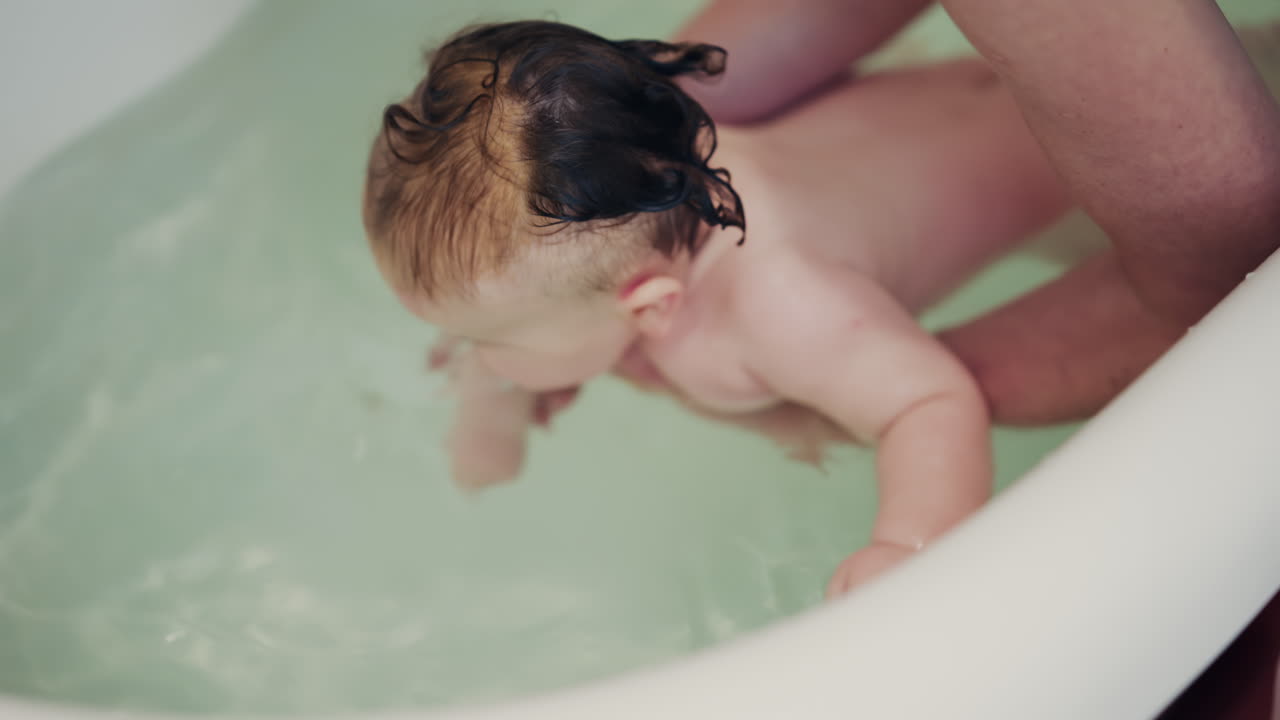 Baby enjoying bath time while being supported by a caregiver