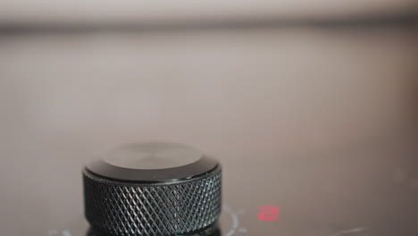 extreme close up of person fingers gripping and turning electric stove knob to activate burner, scene focuses on tactile interaction with textured dial during cooking preparation