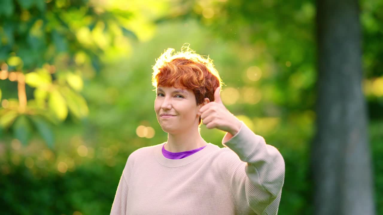 Woman with red hair giving a thumbs up in a park