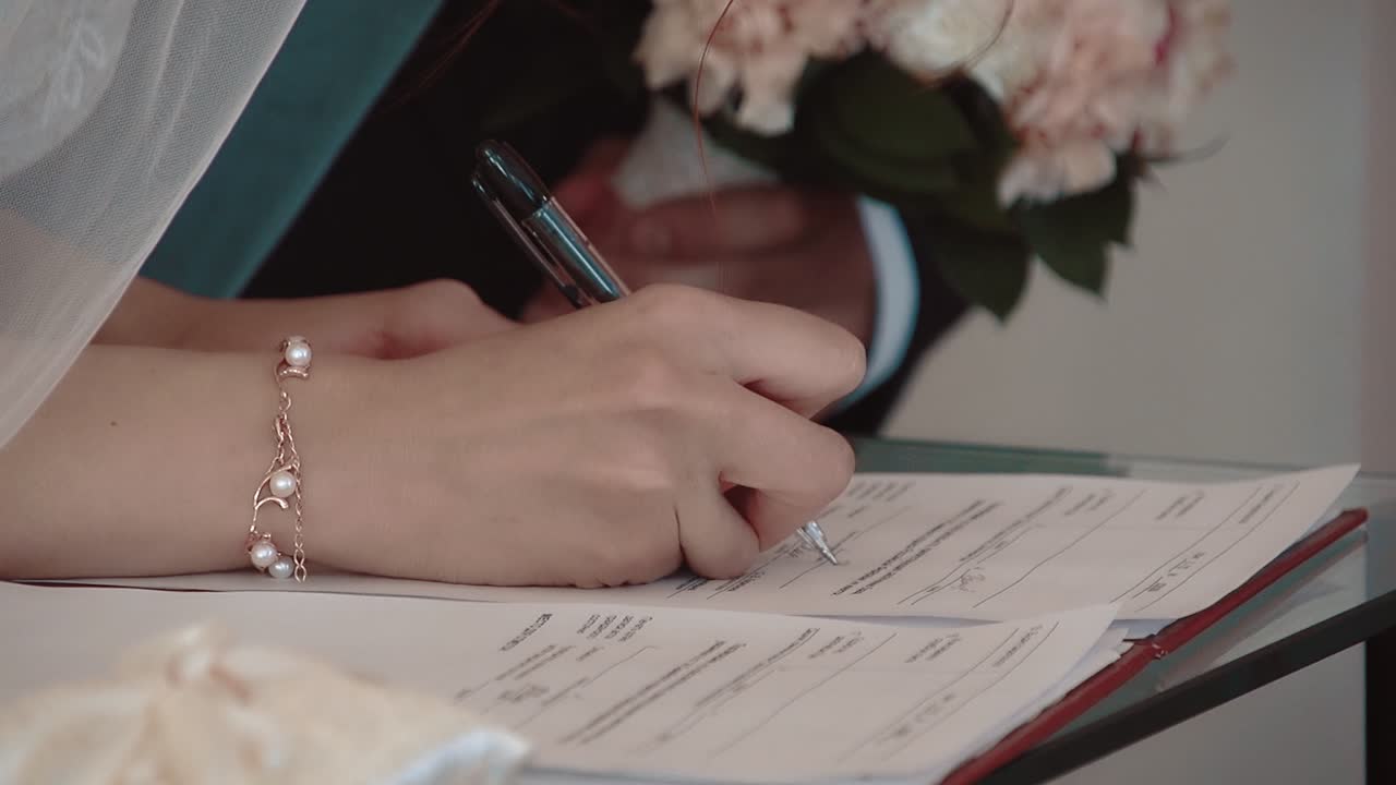 bride signs a marriage contract the groom stands nearby close-up slow motion