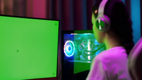 close up of asian teen girl gamer sitting and play video game on computer with mock up green screen