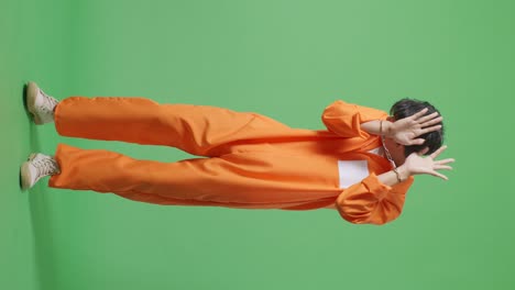 cuerpo lleno de prisionero masculino asiático en esposas de pie en el fondo de la pantalla verde, mostrando la palma de la mano la expresión de no ser querido ser capturado por la cámara