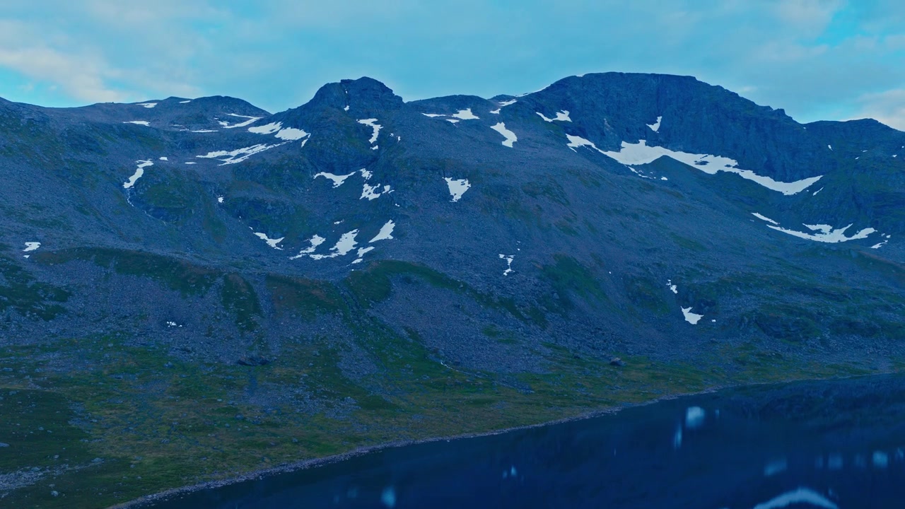 Sør Tverrfjord, Loppa, Norge - En bred udsigt over barske bjerge med snedækkede pletter, der rejser sig over en rolig søbred under en overskyet himmel - Luftfoto fra drone