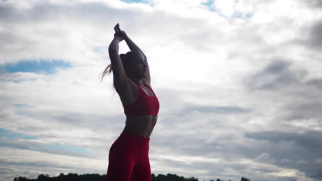 mujer joven en ropa deportiva roja haciendo ejercicios y practicando yoga afuera
