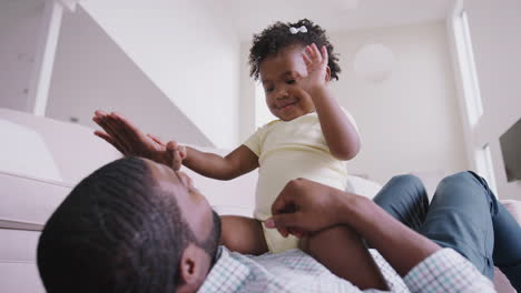 baby daughter sitting on fathers stomach as they play game at home together