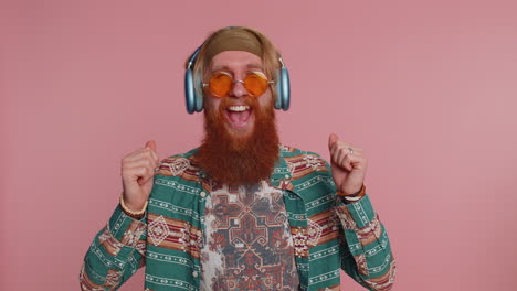 man dancing in a hippie outfit, wearing sunglasses and headphones, on a pink background