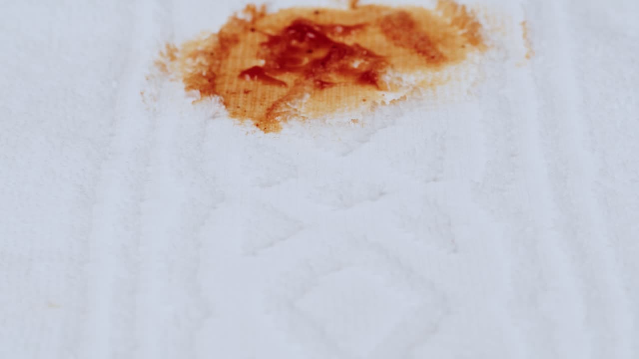 Hnědá tekutina se roztéká a vsakuje do bílé papírové utěrky.