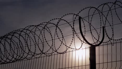 barbed wire hangs on border of a iron fence against the backdrop of sunset. 4k