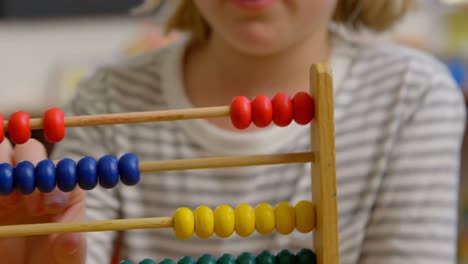 vista frontal de una colegiala caucásica aprendiendo matemáticas con ábaco en el aula 4k