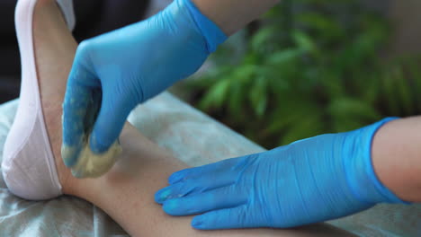 un primer plano de la mano en guantes de goma se aplica a la pasta de depilación y por tecnología especial shugaring elimina el pelo