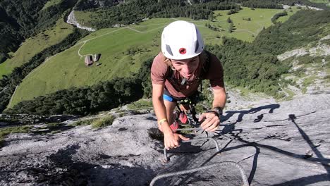 Un-Joven-Blanco-Está-Feliz-Y-Sonriendo-Mientras-Sube-La-Escalera-Hecha-De-Pequeños-Mangos-De-Metal-En-El-Acantilado-De-Una-Montaña-En-Furenalp,-Ferrata-En-Suiza