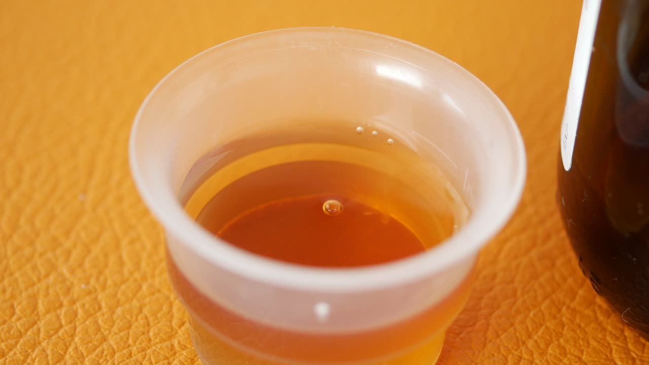 Measuring cup with brown liquid and bottle