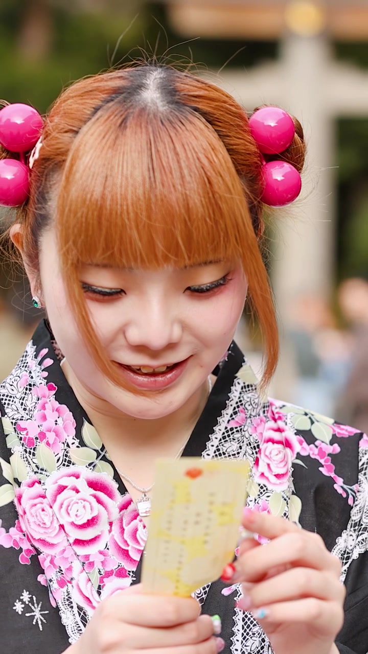 Primo piano di una donna giapponese sorridente che legge un oracolo di carta in un tempio di Tokyo.