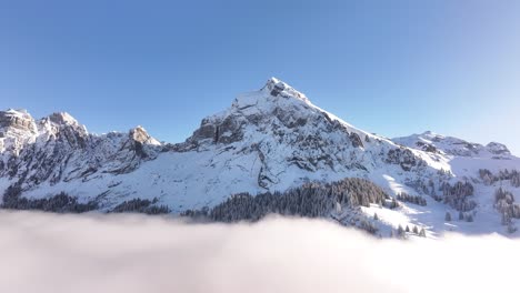 snowy fronalpstock peaks in glarus, switzerland, rise above serene cloud layers, breathtaking drone slowly pulls back, alpine winter scene landscape visuals.