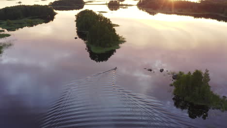 toma de un dron de una lancha navegando lentamente en un lago tranquilo con pequeñas islas al atardecer