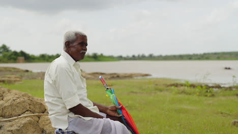 an old man sitting by a lake with an umbrella