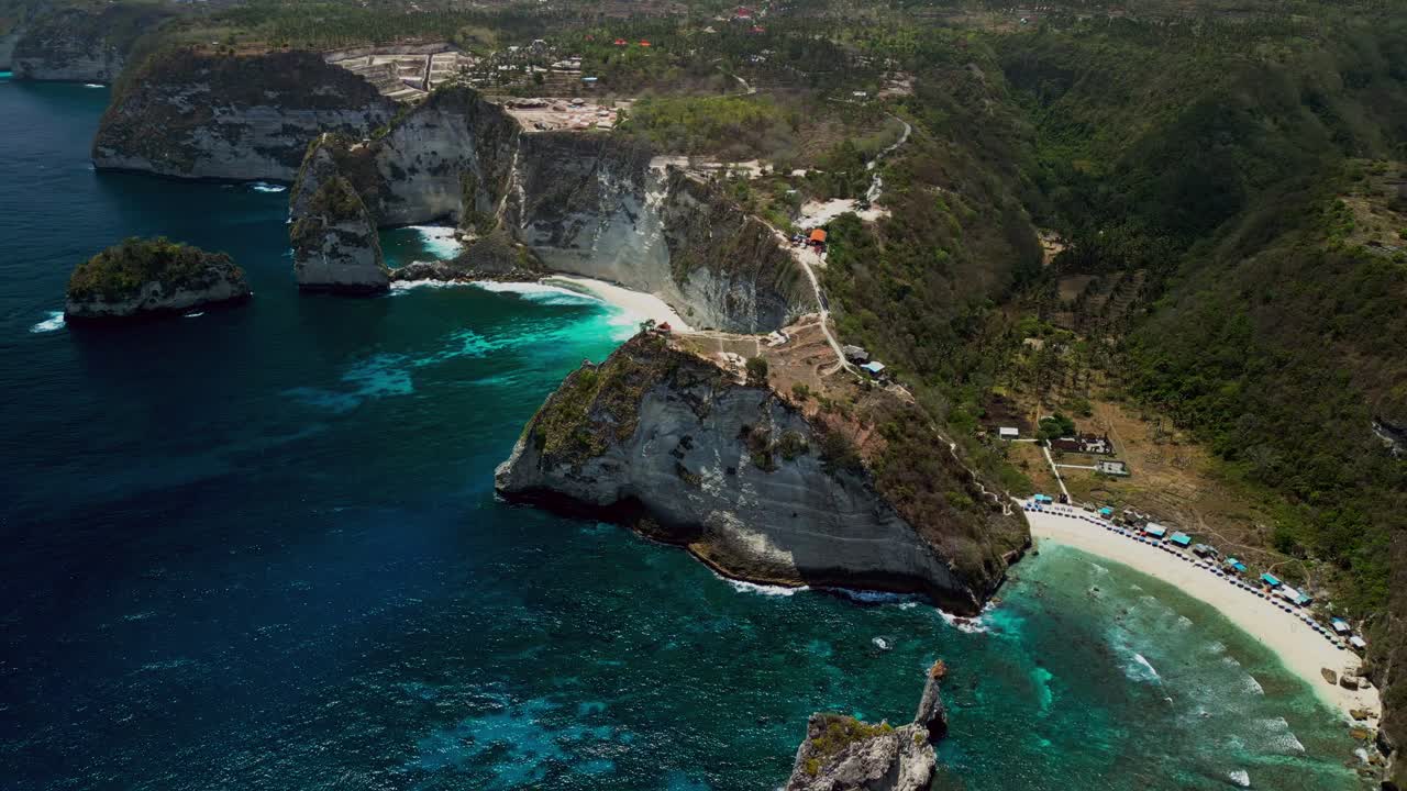 Aerial drone footage of Diamond Beach in Bali shows towering white cliffs and clear blue ocean as sunlight reflects off the water and visitors explore the shore.