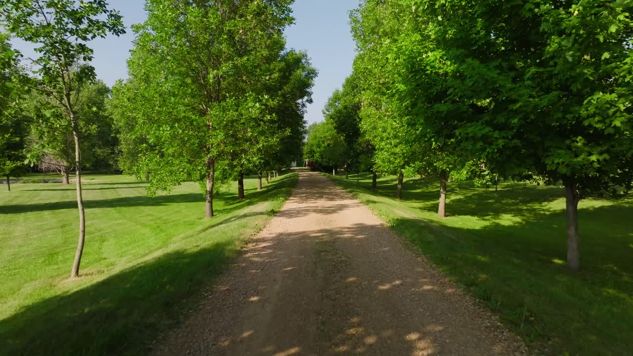 en una toma aérea de un drone de un largo camino de grava rodeado de árboles en un día soleado