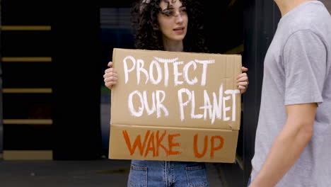 joven hablando con una joven sosteniendo proteger nuestro tablero planetario para protestar 1