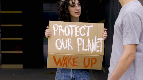 young man talking with young woman holding protect our planet board for protest 1