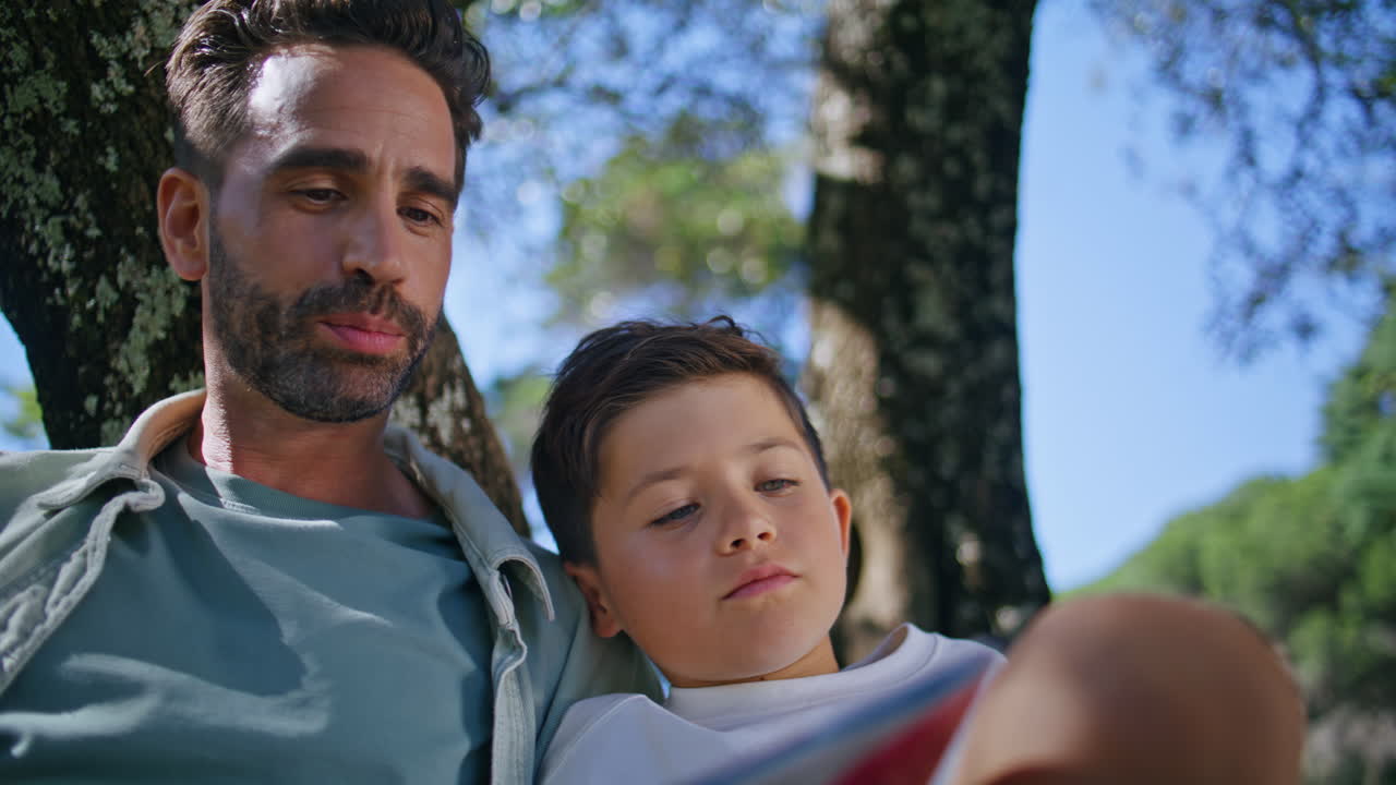 Man boy reading fairytale sitting in forest closeup. Parent little kid resting