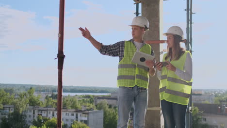 Professional-engineers-in-safety-vests-and-helmets-working-with-digital-tablet-and-blueprints