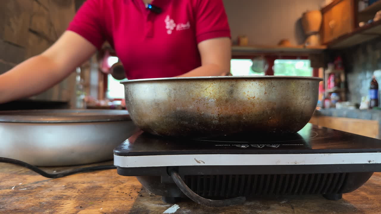 Young woman in red shirt places a bowl on the stove preparing to cook in rustic kitchen