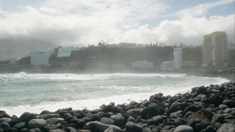 surfistas en cámara lenta esperando en la ola del océano, playa de guijarros cerca de resorts de hoteles, playa martiánez, puerto de la cruz, islas canarias en primavera