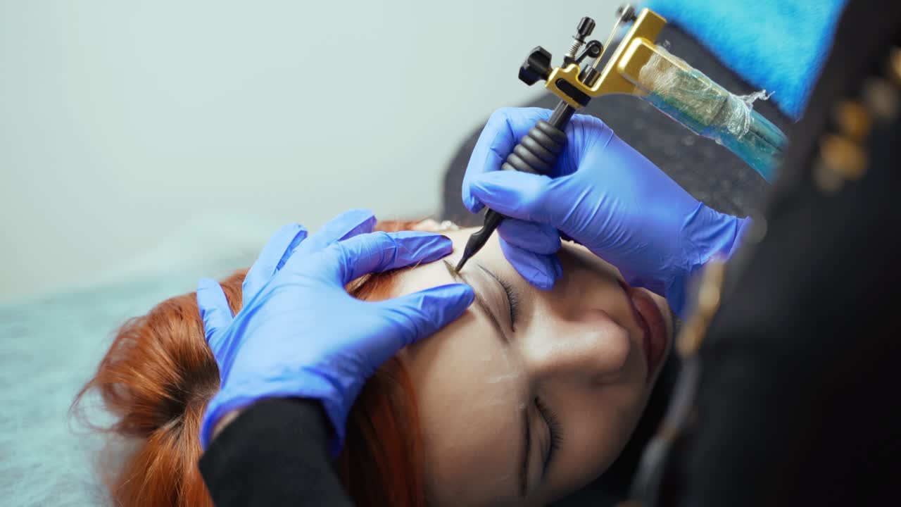 The process of applying permanent makeup on the client's eyebrows in a beauty salon using professional equipment. Close-up