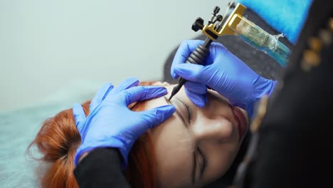 the process of applying permanent makeup on the client's eyebrows in a beauty salon using professional equipment. close-up