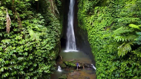 cinematic aerial view : young man trekking to a rock at bottom of leke leke waterfall in tabanan regency in bali, indonesia