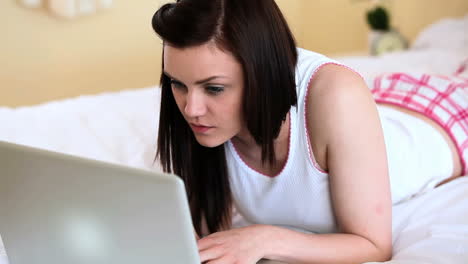 mujer atractiva acostada en la cama usando su computadora portátil