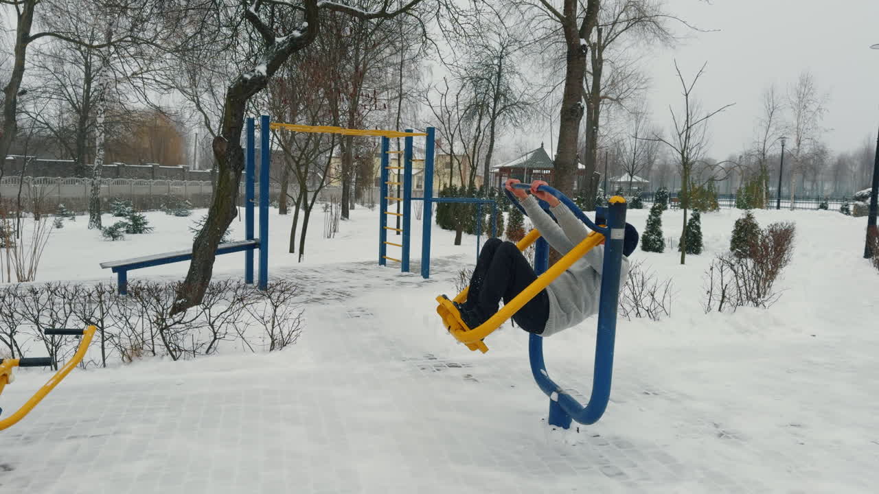 Sportive adult man wearing grey sweater, cap and trousers exercising on simulator. Doing sport outdoors in winter.
