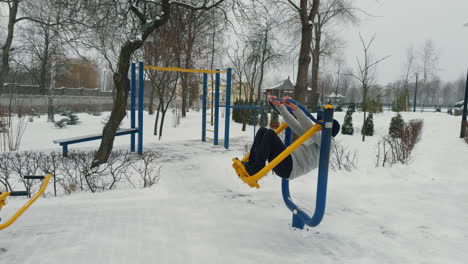 sportive adult man wearing grey sweater, cap and trousers exercising on simulator. doing sport outdoors in winter.