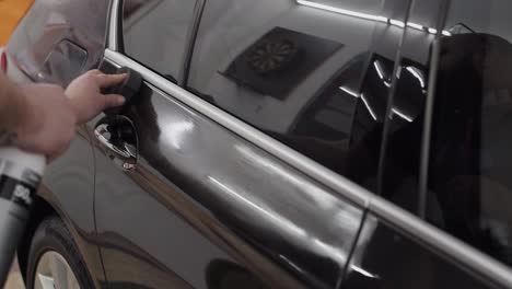 mans hand seen applying cleaning product to car door  during a detailing session