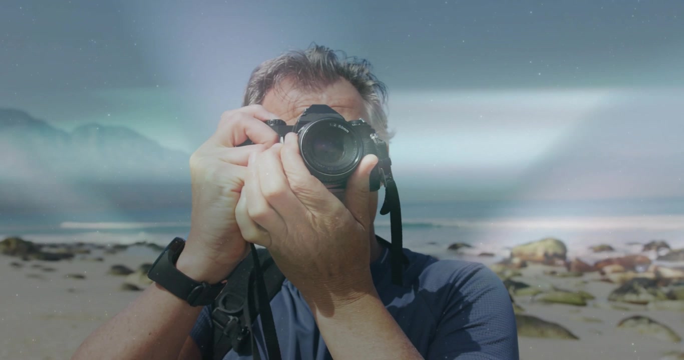 Fotógrafo levando a câmera DSLR ao olho, ajustando o anel de foco e o seletor, capturando fotos de uma costa rochosa