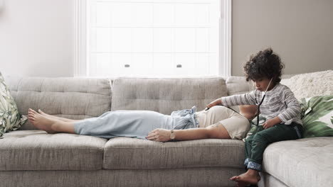 child playing doctor with mother on couch