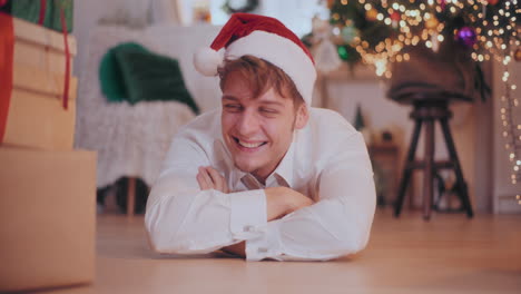 hombre asombrado en sombrero de santa deslizando regalos de navidad mientras yacía en el suelo