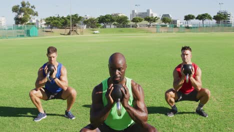 Diverse-group-of-three-fit-men-exercising-outdoors,-squat-lifting-kettlebell-weights