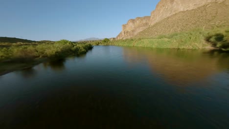 FPV-Aéreo-Volando-Y-Barriendo-Con-Giros-Dramáticos-Sobre-El-Río-Salado-Con-Vista-A-Las-Montañas-Circundantes,-Arbustos-Del-Desierto-En-El-Centro-De-Arizona