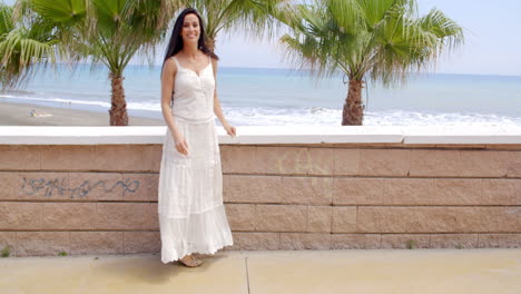 Frau-Im-Weißen-Kleid-An-Der-Wand-Mit-Blick-Auf-Den-Strand