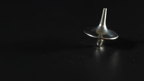 a metallic top spins smoothly on a dark surface, showcasing balance and motion.