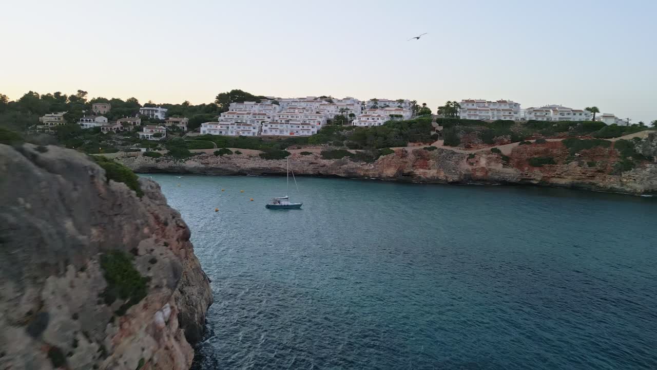 Cala Romántica in Mallorca glimmers at sunset as birds soar gracefully around the rocky cliffs, creating a serene and picturesque coastal scene.